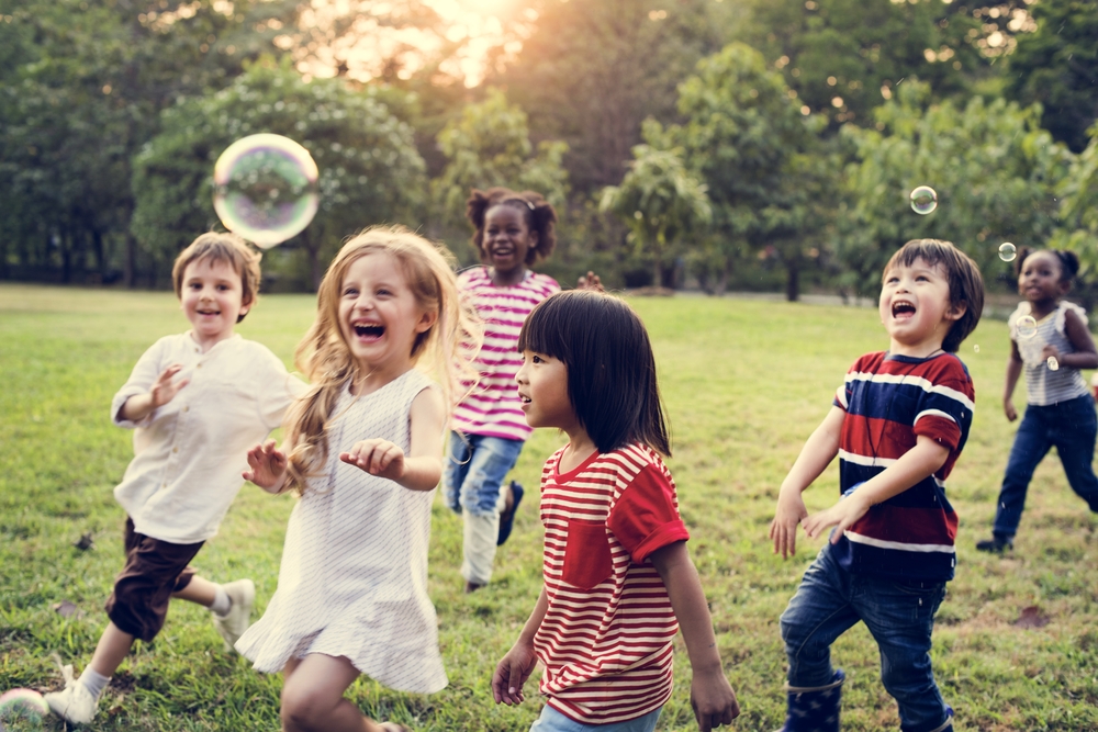 Children Playing In Field With Bubbles